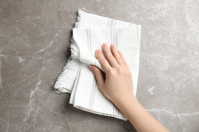 Woman wiping grey marble table with kitchen towel, top view