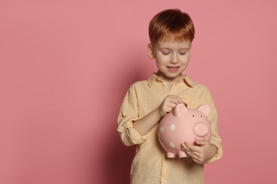 Cute little boy putting coin into piggy bank on pale pink background, space for text