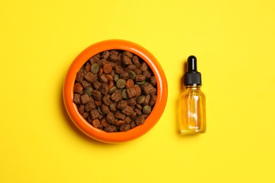 Glass bottle of tincture near bowl with dry pet food on yellow background, flat lay