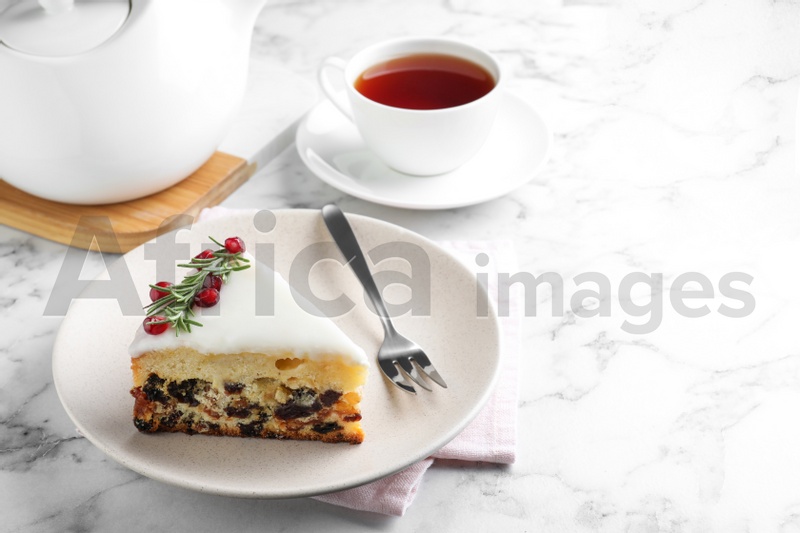 Photo of Slice of traditional Christmas cake decorated with rosemary and pomegranate seeds served on white marble table, space for text