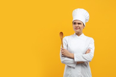 Photo of Upset female chef with wooden spoon on orange background. Space for text