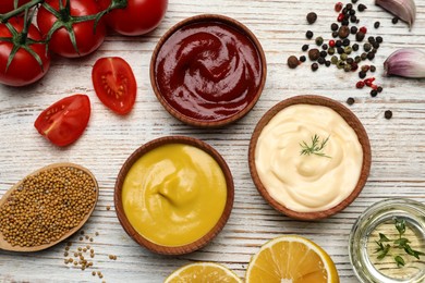 Bowls with mustard, ketchup, mayonnaise and ingredients on wooden table, flat lay