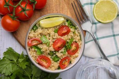 Photo of Delicious quinoa salad with tomatoes, parsley and lime served on white wooden table, flat lay