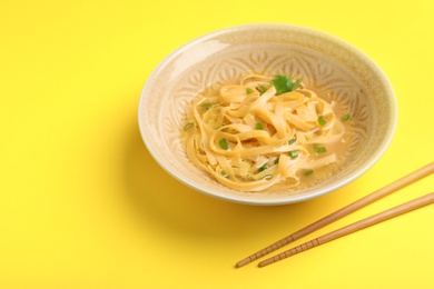 Photo of Cooked noodles with herbs and chopsticks on yellow background