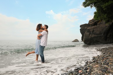 Young couple kissing on beach near sea, space for text