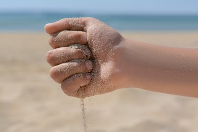 Child pouring sand from hand on beach, closeup. Fleeting time concept