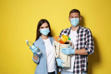 Volunteers in protective masks and gloves with products on yellow background. Aid during coronavirus quarantine