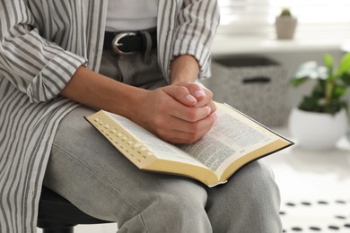 Young woman praying over Bible at home, closeup