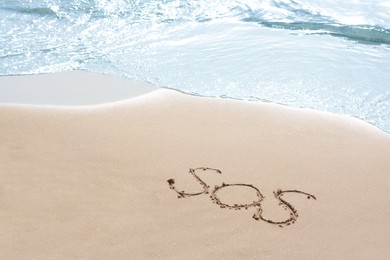 Message SOS drawn on sandy beach near sea