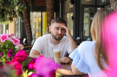 Young man having boring date with girl in outdoor cafe
