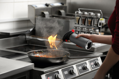 Female chef with manual gas burner cooking tasty food on stove in restaurant kitchen, closeup