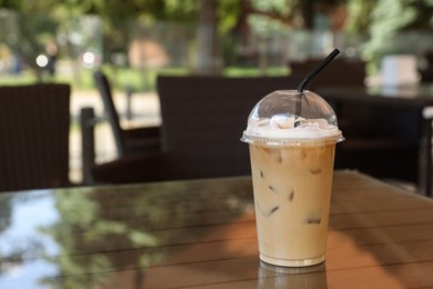 Plastic takeaway cup of delicious iced coffee on table in outdoor cafe, space for text