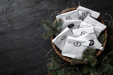 Paper bags, fir branches and garland on black table, flat lay with space for text. Christmas advent calendar