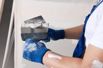 Worker with putty knives and plaster near wall indoors, closeup. Home renovation