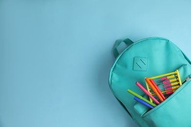 Stylish backpack with different school stationary on light blue background, top view. Space for text