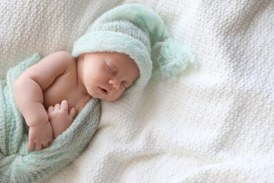 Cute newborn baby in warm hat sleeping on white plaid, above view. Space for text