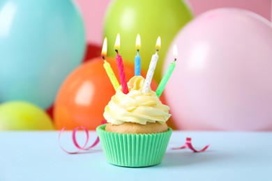 Birthday cupcake with burning candles and streamer on light blue table against color balloons