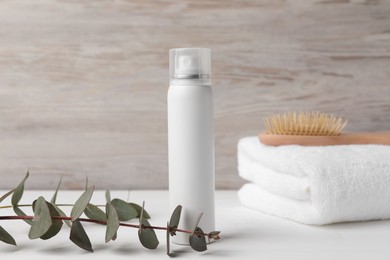 Dry shampoo spray, towel and eucalyptus on white wooden table
