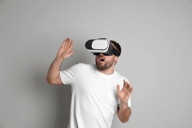 Emotional man using virtual reality headset on light grey background