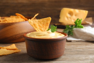 Delicious cheese sauce with nacho and parsley on wooden table, closeup