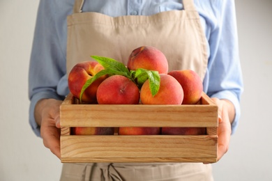 Woman with fresh sweet peaches in wooden crate, closeup