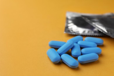 Photo of Pills and condoms on orange background, space for text. Potency problem