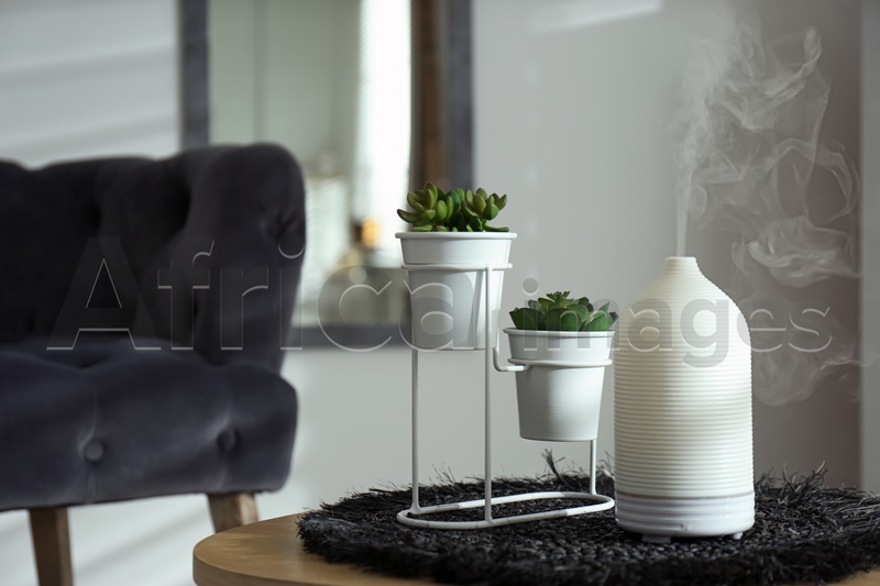 Aroma oil diffuser and houseplant on table in living room. Space for text