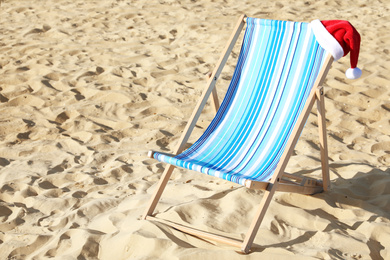 Deck chair with Santa Claus hat on sandy beach. Christmas vacation