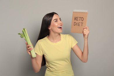 Emotional woman holding celery and notebook with words Keto Diet on light grey background