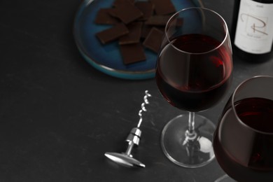 Photo of Tasty red wine and chocolate on black table. Space for text
