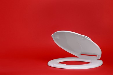 New white plastic toilet seat on red background, space for text