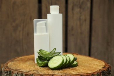 Bottles of cosmetic products, sliced aloe vera leaves and cucumber on wooden stump