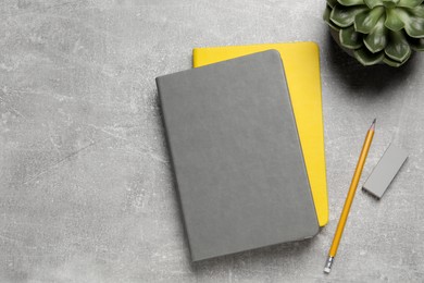Notebooks, plant, pencil and eraser on light grey table, flat lay