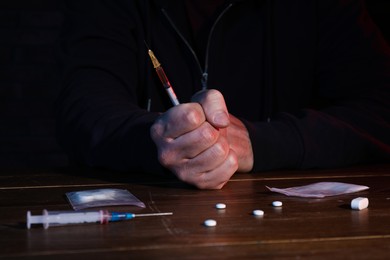 Drug addicted man holding syringe at table, closeup