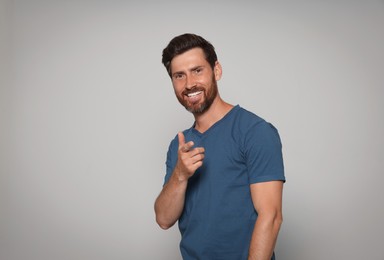 Smiling bearded man pointing forward finger on grey background. Space for text