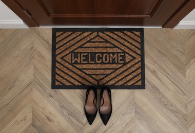 Stylish female shoes near door mat in hall, top view