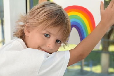 Little boy holding rainbow painting near window. Stay at home concept