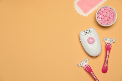 Modern epilator and other hair removal products on orange background, flat lay. Space for text