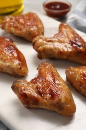 Photo of Delicious fried chicken wings on white marble board, closeup