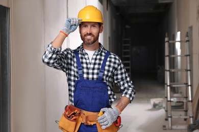 Professional builder in uniform with tool belt indoors