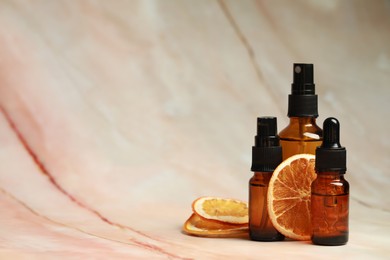 Bottles of organic cosmetic products and dried orange slices on marbled background, space for text