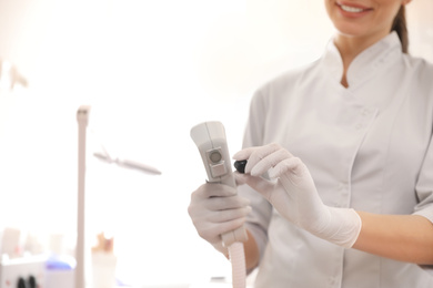 Young woman holding professional laser epilator in beauty salon, closeup