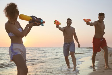 Friends with water guns having fun on beach at sunset