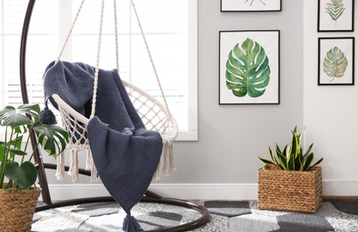 Stylish room interior with artworks and hanging chair