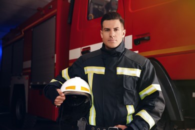 Portrait of firefighter in uniform with helmet near fire truck at station