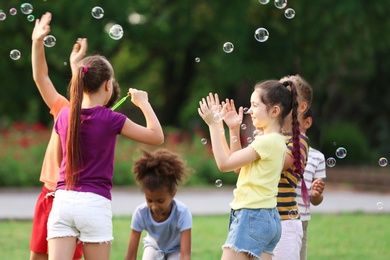 Cute little children playing with soap bubbles in park