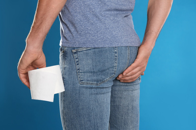 Man with toilet paper suffering from hemorrhoid on light blue background, closeup