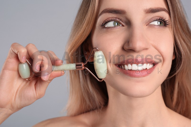 Photo of Young woman using natural jade face roller on light grey background, closeup