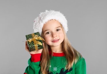 Cute child in Santa hat with Christmas gift on grey background