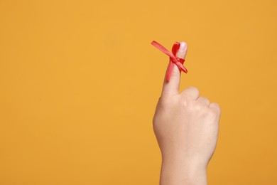 Man showing index finger with red tied bow as reminder on orange background, closeup. Space for text